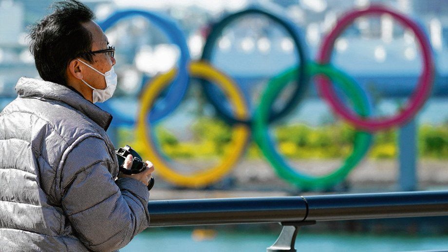 A visitor wearing a face mask stands near the Olympic rings at Tokyo'
